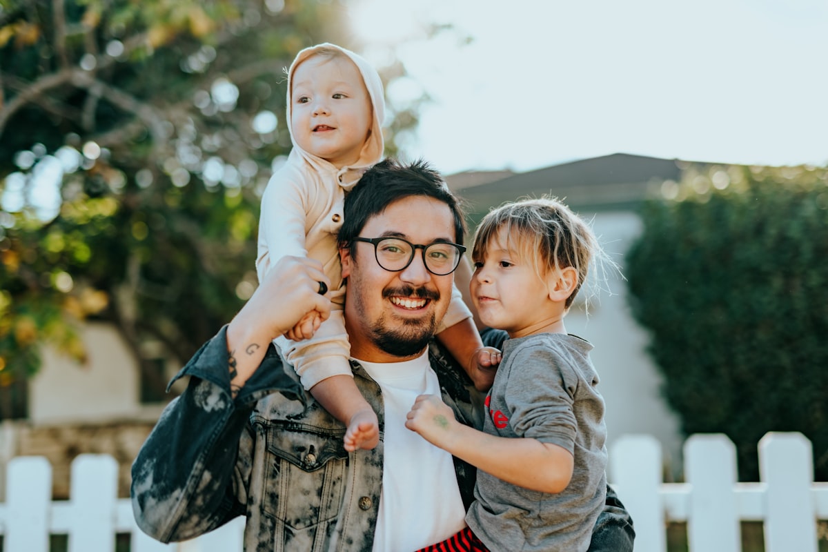 Un papa porte ses deux enfants sur les épaules dans le jardin